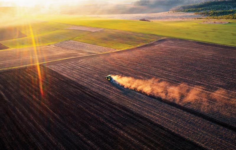 Tractor driving across a field with dust in it's trail